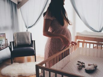 woman in white lace sleeveless dress standing beside brown wooden crib
