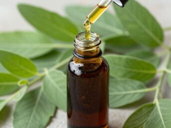 Patchouli oil pouring from dropper into vial with leaves.