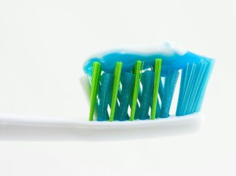 white, blue, and green toothbrush with blue toothpaste, clove oil for toothache